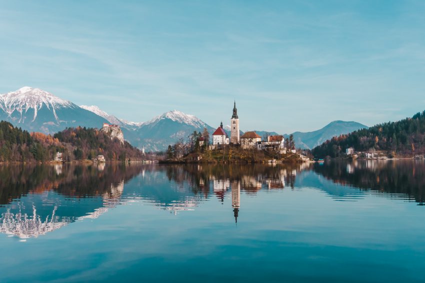 Church on an island in the middle of Lake Bled, with snow-capped mountains in the background.